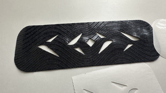 Back of an Easy Tape pre-cut kinesiology tape strip showing the wave-pattern fabric and diamond cut-outs, with the peeled backing beside it