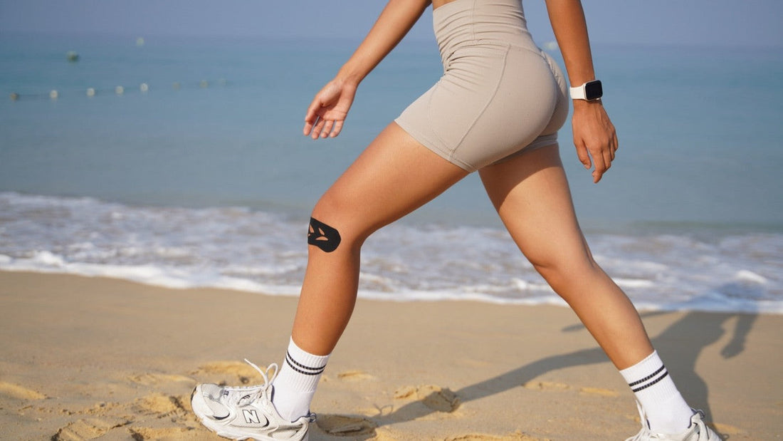 Woman walking on a beach with a black pre-cut Easy Tape kinesiology strip supporting her knee