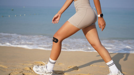 Woman walking on a beach with a black pre-cut Easy Tape kinesiology strip supporting her knee